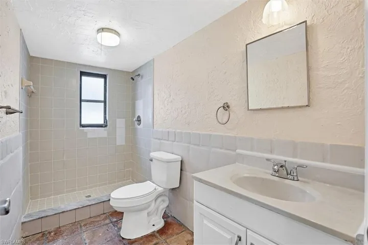 Bathroom featuring a textured wall, vanity, wainscoting, a textured ceiling, and tile walls