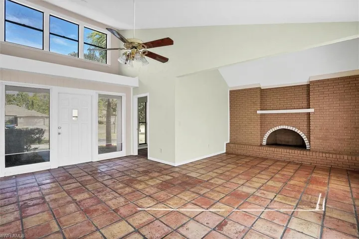 Unfurnished living room featuring healthy amount of natural light, high vaulted ceiling, a brick fireplace, and ceiling fan