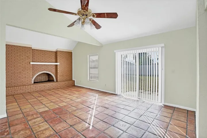 Unfurnished living room with a fireplace, a ceiling fan, brick wall, and vaulted ceiling
