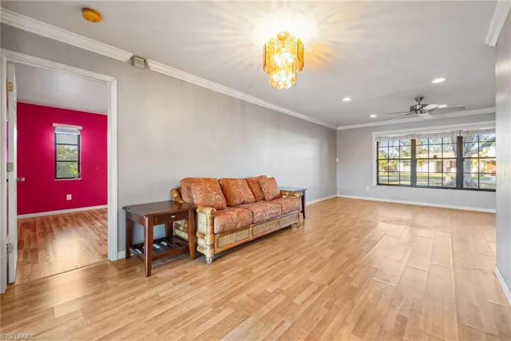 Living area with crown molding, light wood-type flooring, a ceiling fan, a chandelier, and plenty of natural light