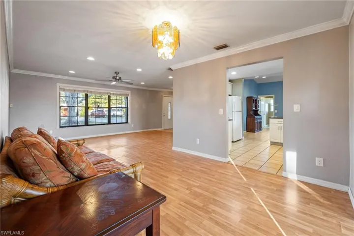 Living area with light wood-style floors, hanging lights, a ceiling fan, and crown molding