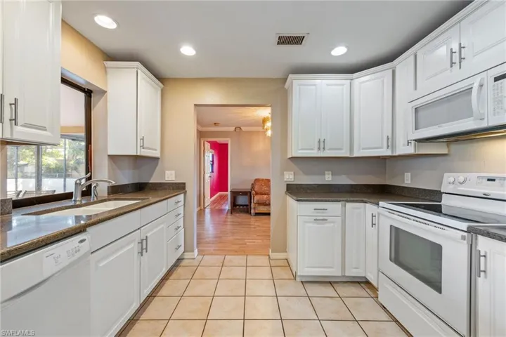 Kitchen with white appliances, white cabinetry, dark stone countertops, recessed lighting, and light tile patterned floors