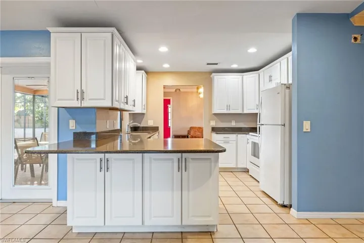 Kitchen with a peninsula, white cabinets, white appliances, dark stone counters, and light tile patterned floors