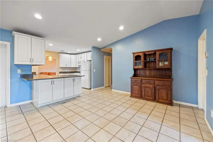 Kitchen with dark countertops, a peninsula, freestanding refrigerator, recessed lighting, and white cabinets