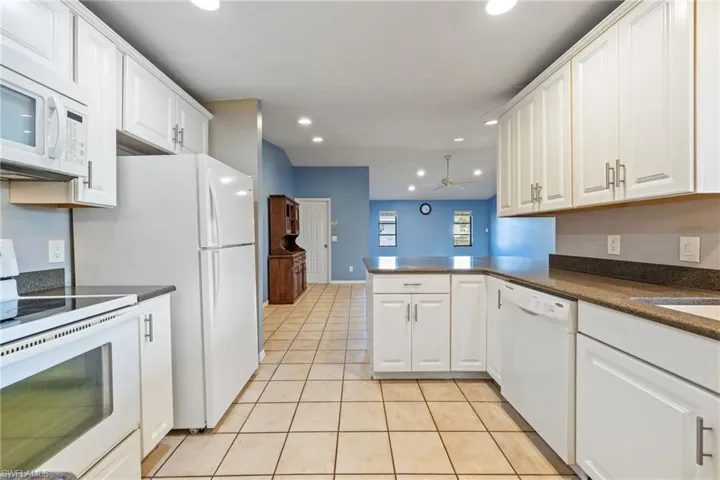 Kitchen with white appliances, a peninsula, light tile patterned floors, white cabinets, and recessed lighting