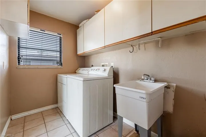 Laundry area featuring washer and dryer, light tile patterned floors, and cabinet space