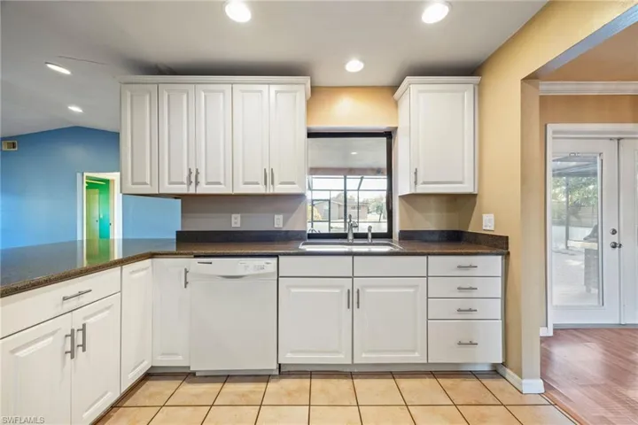Kitchen with white dishwasher, white cabinets, dark stone countertops, and recessed lighting