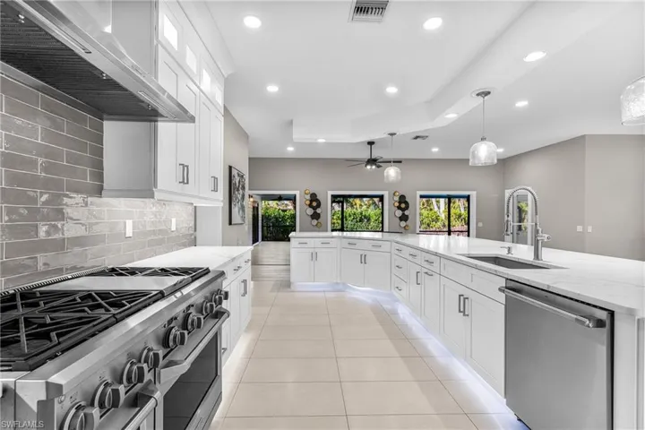 Kitchen featuring tasteful backsplash, high end appliances, wall chimney range hood, white cabinetry, and recessed lighting