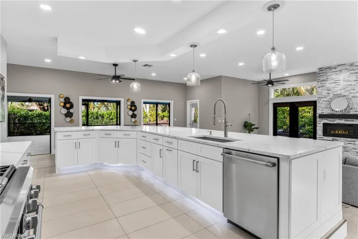 Kitchen featuring wall chimney range hood, appliances with stainless steel finishes, a raised ceiling, ceiling fan, and recessed lighting