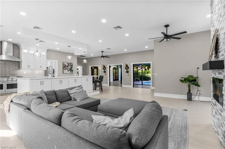 Kitchen with a ceiling fan, open floor plan, appliances with stainless steel finishes, a large fireplace, and white cabinetry