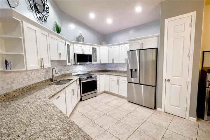 Kitchen with light stone countertops, appliances with stainless steel finishes, white cabinets, backsplash, and lofted ceiling