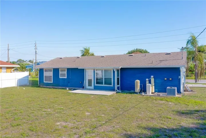 Back of property with cooling unit, a patio area, fence, and a lawn