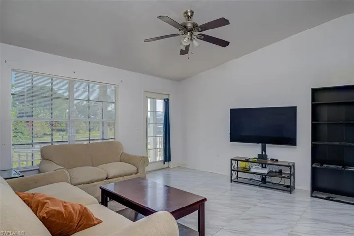 Living area with ceiling fan, marble finish floor, vaulted ceiling, and baseboards