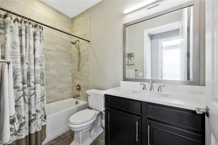 Full bathroom featuring wood finished floors, vanity, toilet, and shower / bathtub combination with curtain