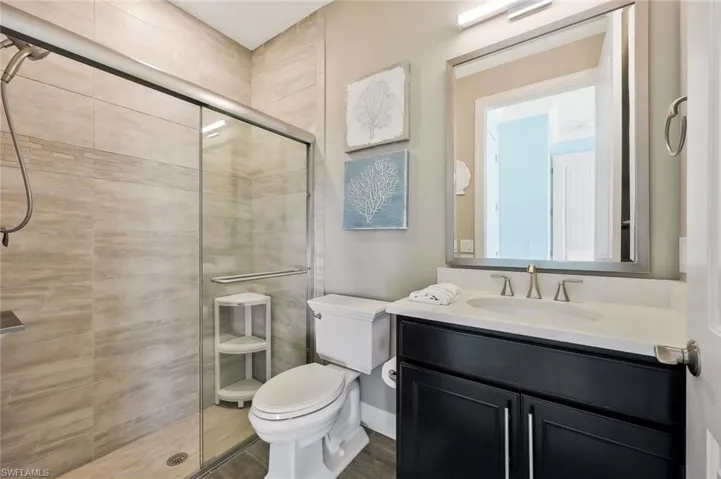 Bathroom with wood finished floors, a stall shower, vanity, and toilet