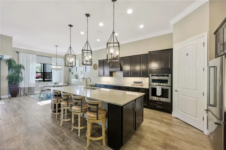 Kitchen featuring a center island with sink, stainless steel appliances, tasteful backsplash, a sink, and light wood-type flooring