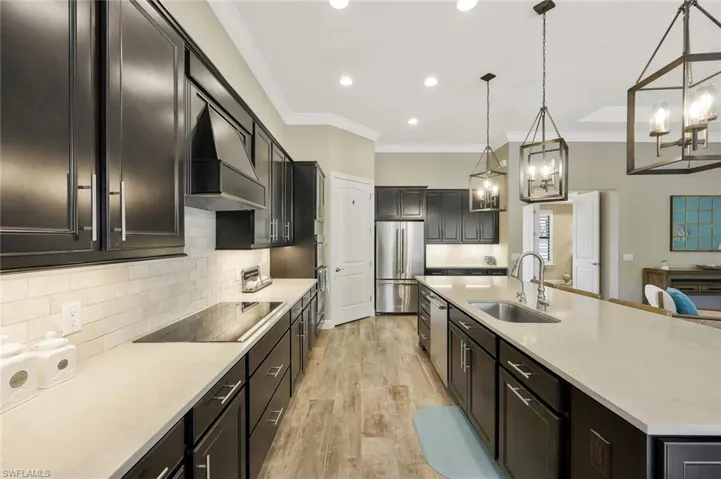 Kitchen featuring a sink, light wood-style floors, ornamental molding, appliances with stainless steel finishes, and custom exhaust hood