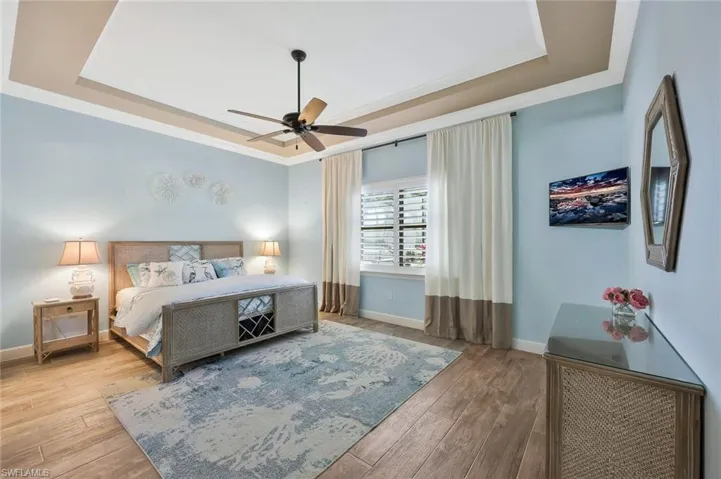 Bedroom with ornamental molding, a raised ceiling, and wood finished floors