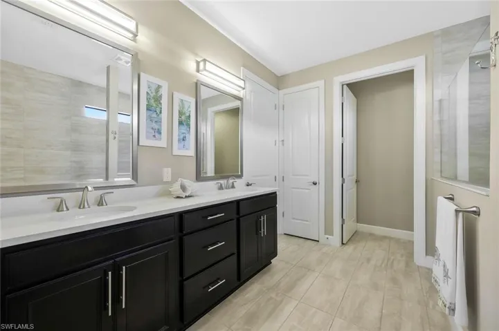 Full bathroom with a tile shower, double vanity, a sink, and baseboards