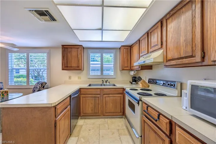 Kitchen featuring under cabinet range hood, brown cabinetry, visible vents, a peninsula, and white appliances