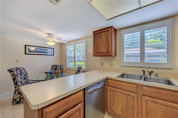 Kitchen with stainless steel dishwasher, light countertops, brown cabinets, a sink, and a peninsula