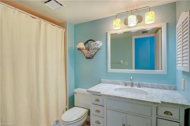 Bathroom with toilet, visible vents, vanity, and curtained shower