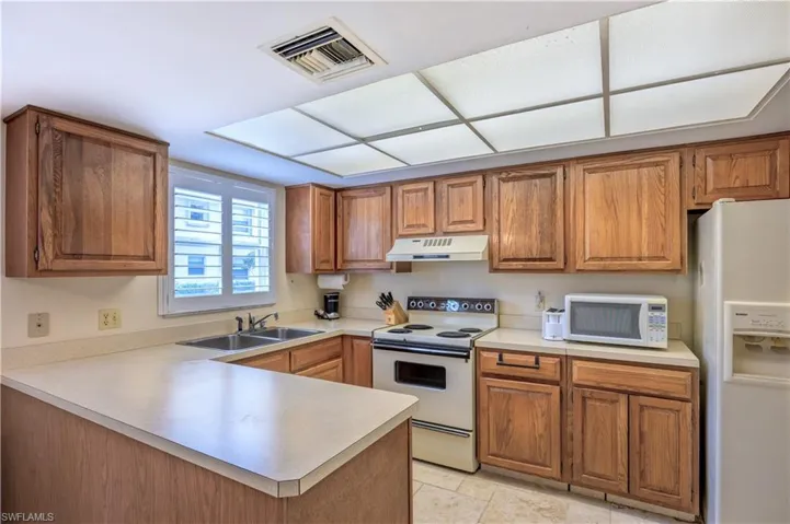Kitchen with visible vents, light countertops, a peninsula, white appliances, and brown cabinetry