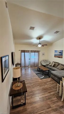 Vaulted ceiling, wood-finish flooring, ceiling fan, and sliding glass door with privacy curtains