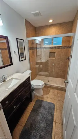 Tiled bathroom featuring a dark wood-finish vanity with a light-toned countertop, a glass-enclosed shower with tile surround, and recessed lighting