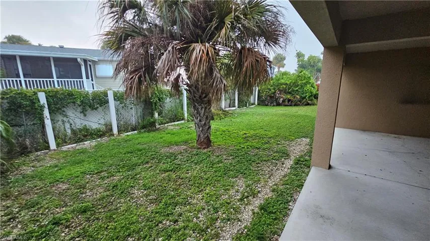 Expansive outdoor living area with a covered patio, a mature palm tree, and a grassy lawn