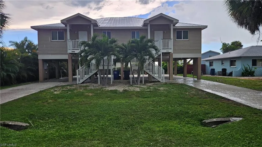 Elevated coastal-style architecture featuring a metal roof, dual exterior staircases, and mature palm trees