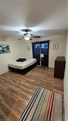 Wood-finish flooring with a ceiling fan light fixture and window with dark drapery