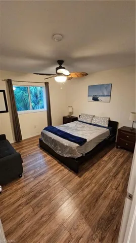 Wood-finish flooring throughout, ceiling fan with integrated lighting, and a large window with privacy curtains