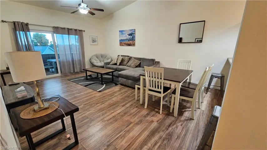 Vaulted ceiling with ceiling fan, wood-finish flooring, sliding glass door, and a built-in wall shelf
