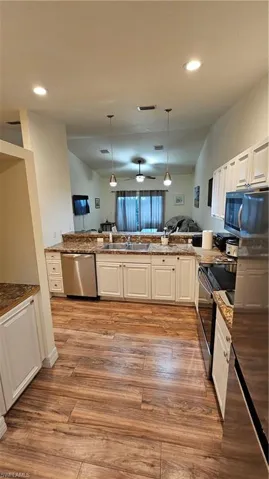 Kitchen featuring wood-finish flooring, white cabinetry, stainless steel appliances, and pendant lighting