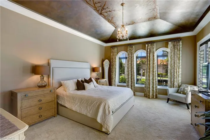 Bedroom with a chandelier, light carpet, multiple windows, ornamental molding, and a hand painted tray ceiling