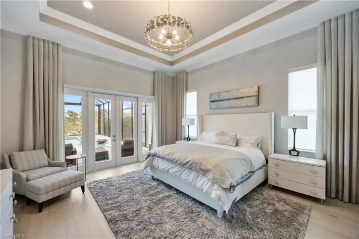 Bedroom featuring a raised ceiling, access to outside, multiple windows, a chandelier, and a high ceiling