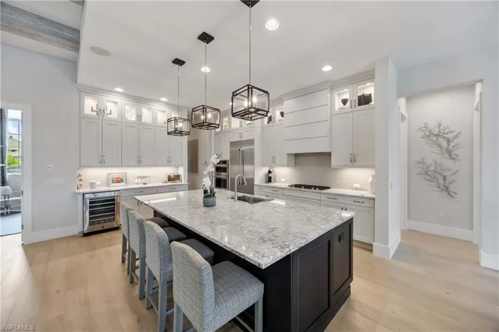 Kitchen featuring glass insert cabinets, light stone countertops, backsplash, a kitchen breakfast bar, and white cabinetry