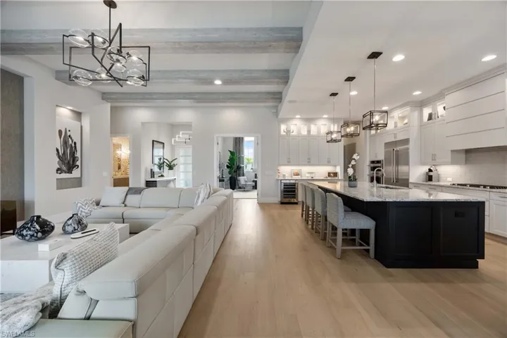 Living area featuring a chandelier, beamed ceiling, light wood-style floors, recessed lighting, and wine cooler