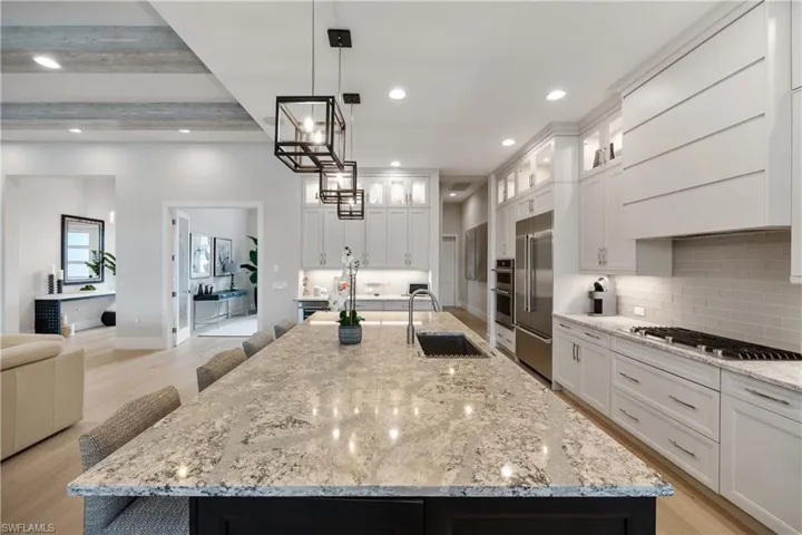 Kitchen featuring a kitchen bar, light wood-type flooring, a spacious island, light stone countertops, and beamed ceiling