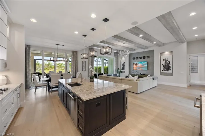 Kitchen with beamed ceiling, white cabinets, light wood finished floors, light stone counters, and hanging light fixtures