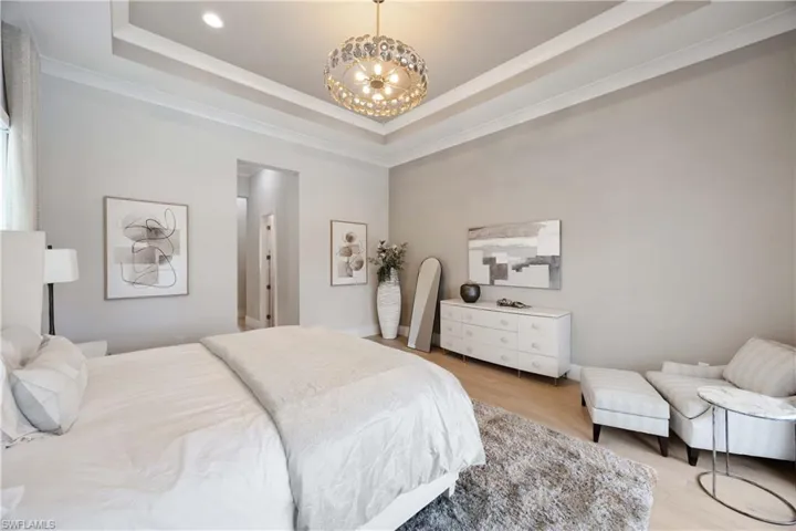 Bedroom featuring a tray ceiling, a chandelier, ornamental molding, and wood finished floors