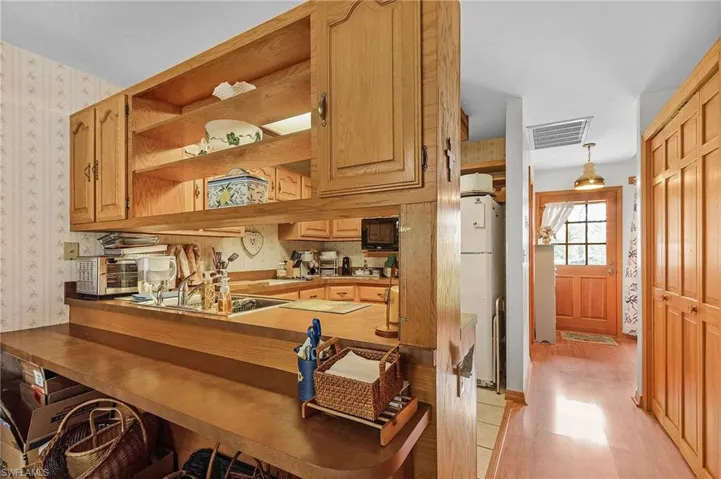 Bar featuring wallpapered walls, freestanding refrigerator, black microwave, light wood-style floors, and cooktop