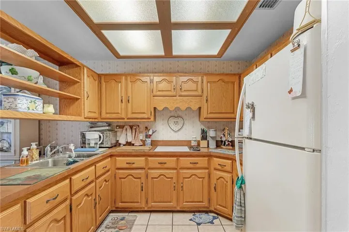 Kitchen featuring freestanding refrigerator, wallpapered walls, light tile patterned floors, and open shelves
