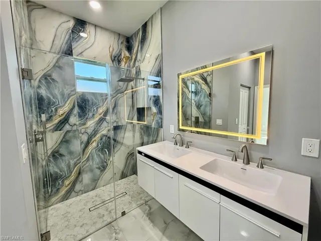 Full bathroom featuring double vanity, light marble finish flooring, and a marble finish shower