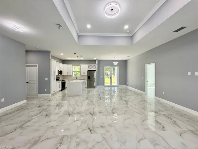 Unfurnished living room featuring french doors, a tray ceiling, light marble finish floors, recessed lighting, and ornamental molding