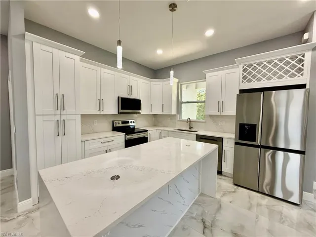 Kitchen with stainless steel appliances, light marble finish floors, a center island, hanging light fixtures, and light stone countertops
