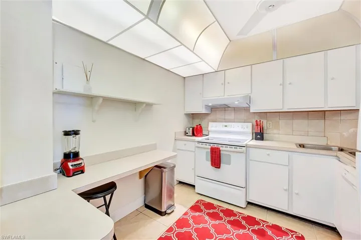 Kitchen featuring white range with electric stovetop, backsplash, light countertops, white cabinets, and light tile patterned floors