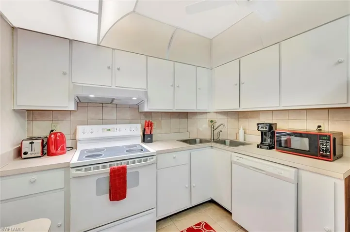 Kitchen with white appliances, light countertops, white cabinetry, and backsplash