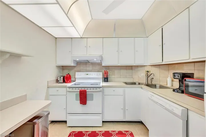 Kitchen featuring white appliances, decorative backsplash, light countertops, and white cabinetry